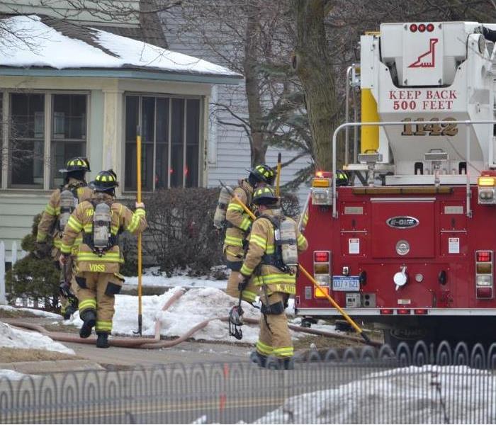 Four firefighters and a firetruck outside a house.